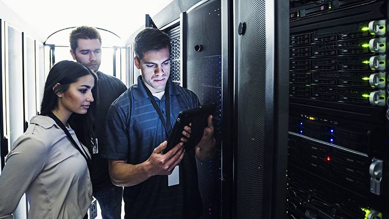 Two young men and young woman looking at tablet computer in datacenter