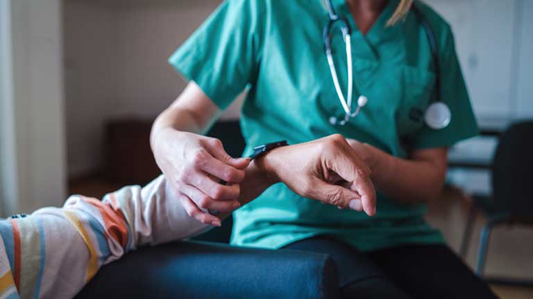 Medical worker puts a smartwatch used for remote monitoring on a patient’s wrist
