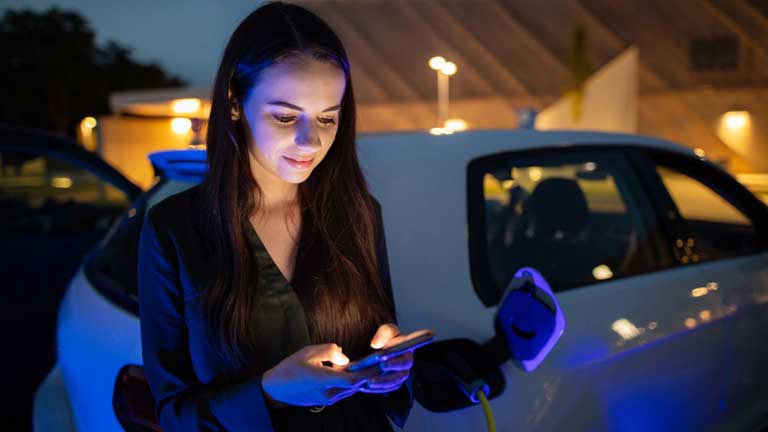 Woman using cell phone to connect with her electric vehicle